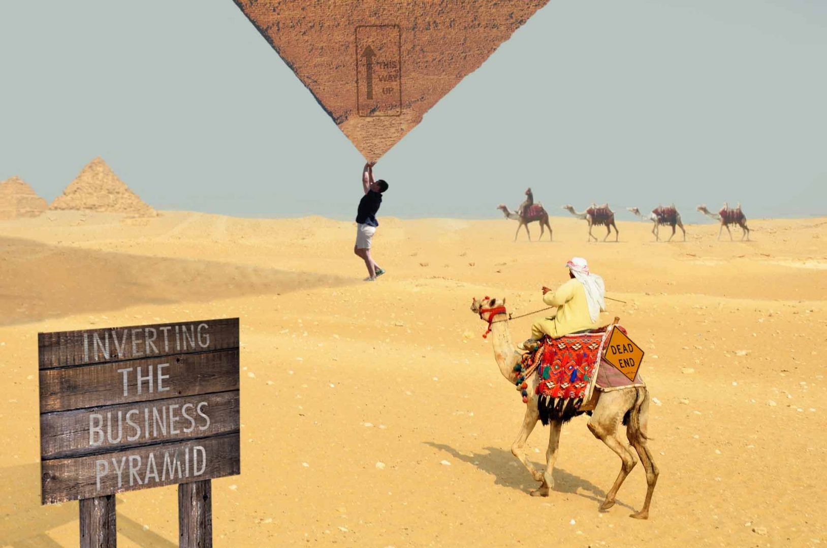 Standing in the desert lifting and inverting the big business pyramid upside down amongst the surprised camel riders